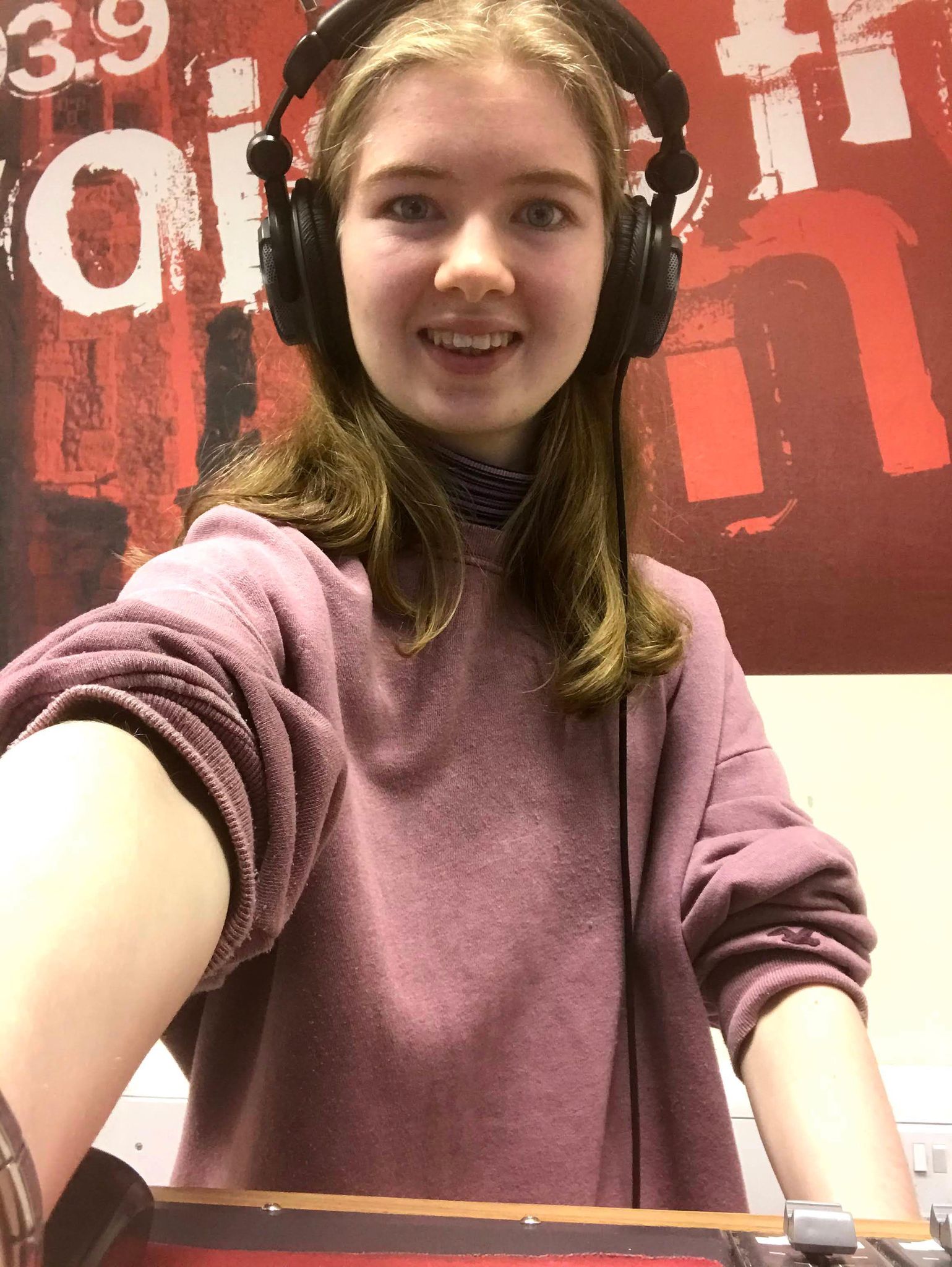 Selfie of Kate in the Voice FM studio with headphones on her head and a pink jumper on